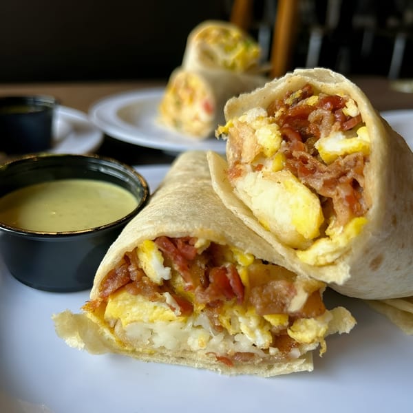 Two Cabaña Mexican Grill breakfast burritos, one cut open, with a side of green sauce.