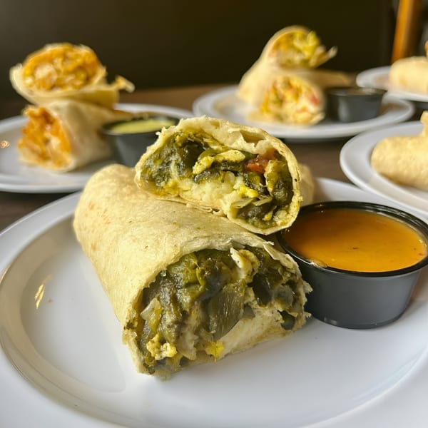 A Cabaña Mexican Grill burrito, cut in half to show a green filling, with a side of orange sauce.