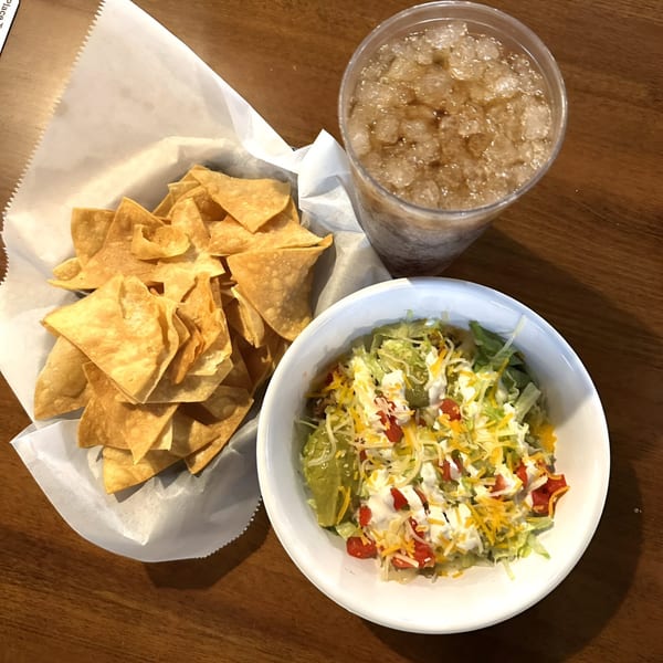 Cabaña Mexican Grill's taco salad with chips and a drink on a wooden table.