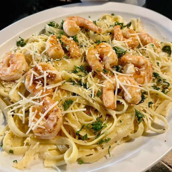 Shrimp fettuccine alfredo with grated cheese and parsley on a white oval plate.