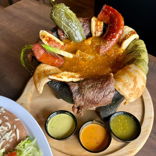 A Cabaña Mexican Grill molcajete with meat, cheese, peppers, and sauce, served with three dipping sauces.