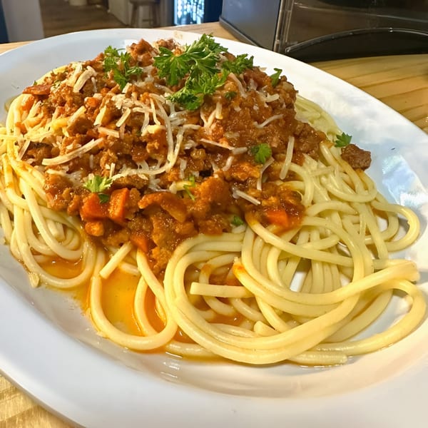 Spaghetti with meat sauce, shredded cheese, and parsley on a white oval plate.