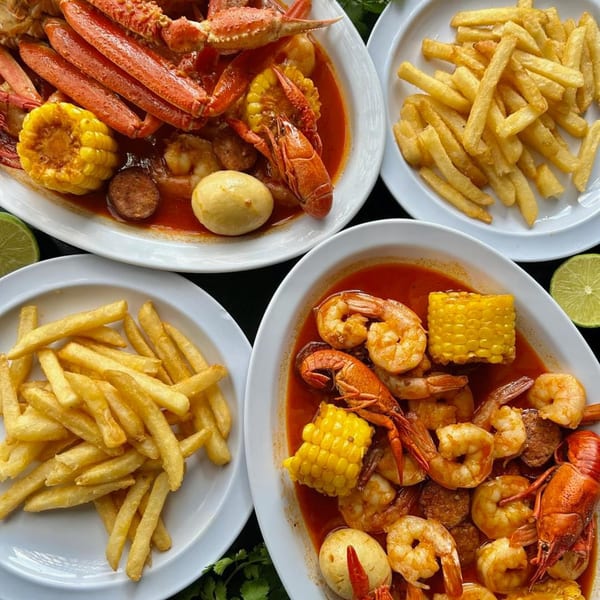 Two plates of seafood boil with crab legs, shrimp, crawfish, corn, and potatoes, alongside two plates of fries.